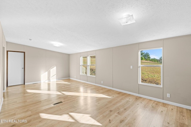 empty room featuring a textured ceiling, light hardwood / wood-style flooring, and basketball hoop