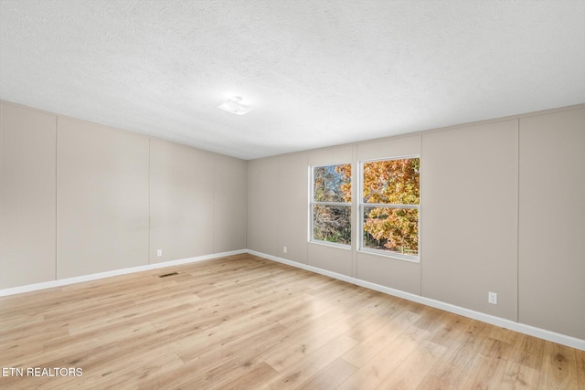 spare room with a textured ceiling and light hardwood / wood-style flooring