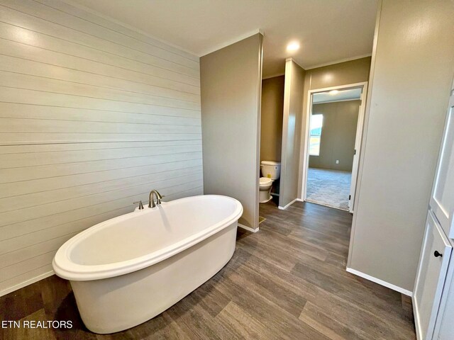 bathroom featuring a bath, hardwood / wood-style flooring, toilet, and wood walls