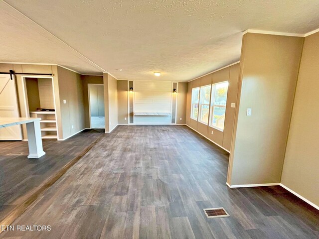 unfurnished living room featuring a textured ceiling, dark hardwood / wood-style flooring, a barn door, and crown molding