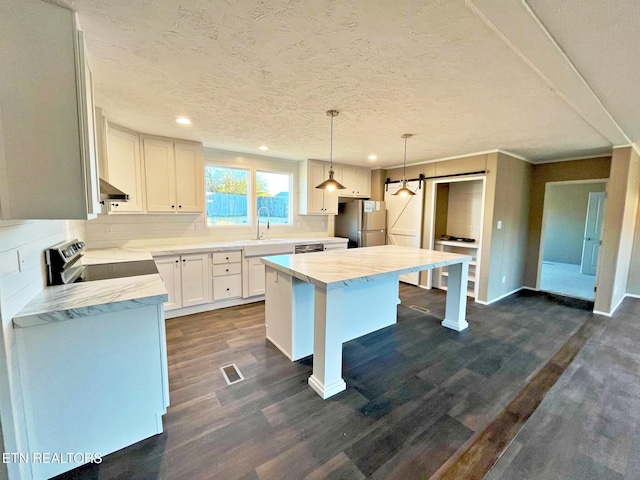 kitchen with hanging light fixtures, a barn door, dark hardwood / wood-style flooring, white cabinetry, and stainless steel appliances