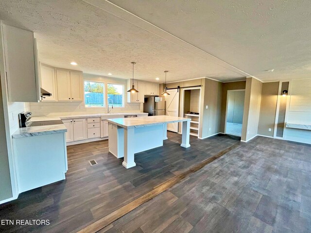 kitchen featuring appliances with stainless steel finishes, a barn door, a center island, and white cabinetry