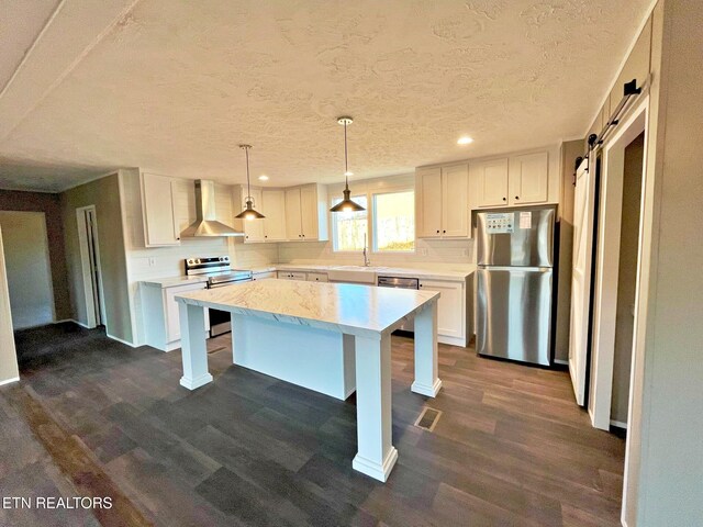 kitchen with wall chimney exhaust hood, stainless steel appliances, dark wood-type flooring, a barn door, and a center island