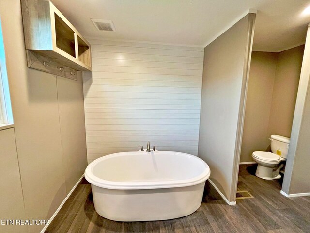 bathroom with hardwood / wood-style flooring, a bathtub, toilet, and wooden walls