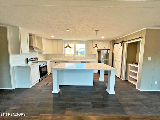 kitchen featuring pendant lighting, a center island, wall chimney range hood, a barn door, and appliances with stainless steel finishes