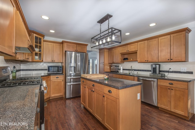 kitchen with a kitchen island, appliances with stainless steel finishes, decorative light fixtures, sink, and dark stone counters