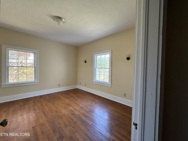 empty room with a wealth of natural light, dark wood-type flooring, and a textured ceiling