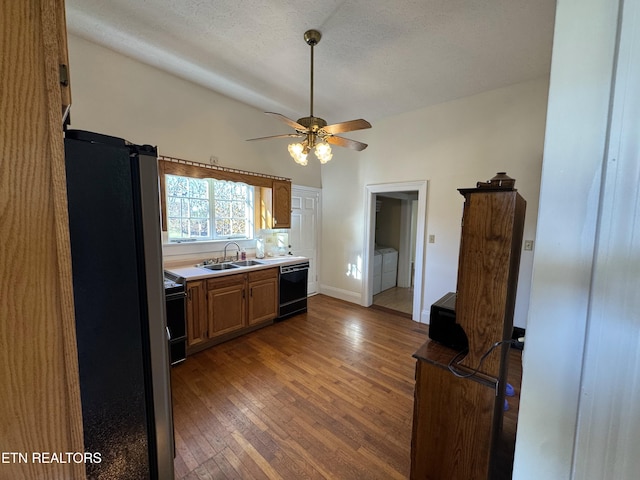 kitchen with washing machine and clothes dryer, ceiling fan, sink, dark hardwood / wood-style floors, and black appliances