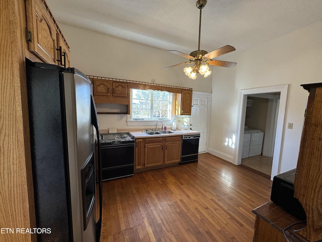 kitchen featuring washing machine and clothes dryer, ceiling fan, sink, dark wood-type flooring, and black appliances