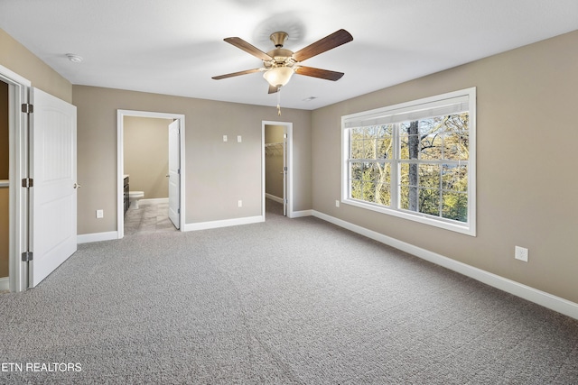 unfurnished bedroom featuring light carpet, ceiling fan, a spacious closet, connected bathroom, and a closet