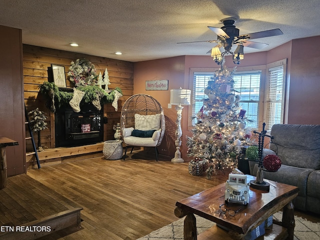 living room featuring ceiling fan, wood walls, a textured ceiling, and hardwood / wood-style flooring