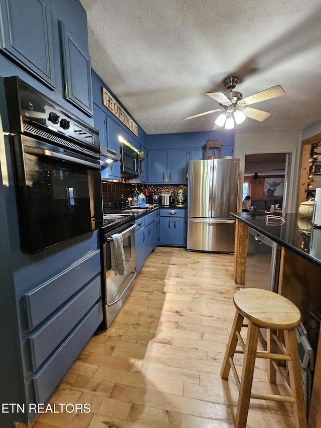 kitchen with blue cabinetry, stainless steel appliances, light hardwood / wood-style flooring, a textured ceiling, and decorative backsplash