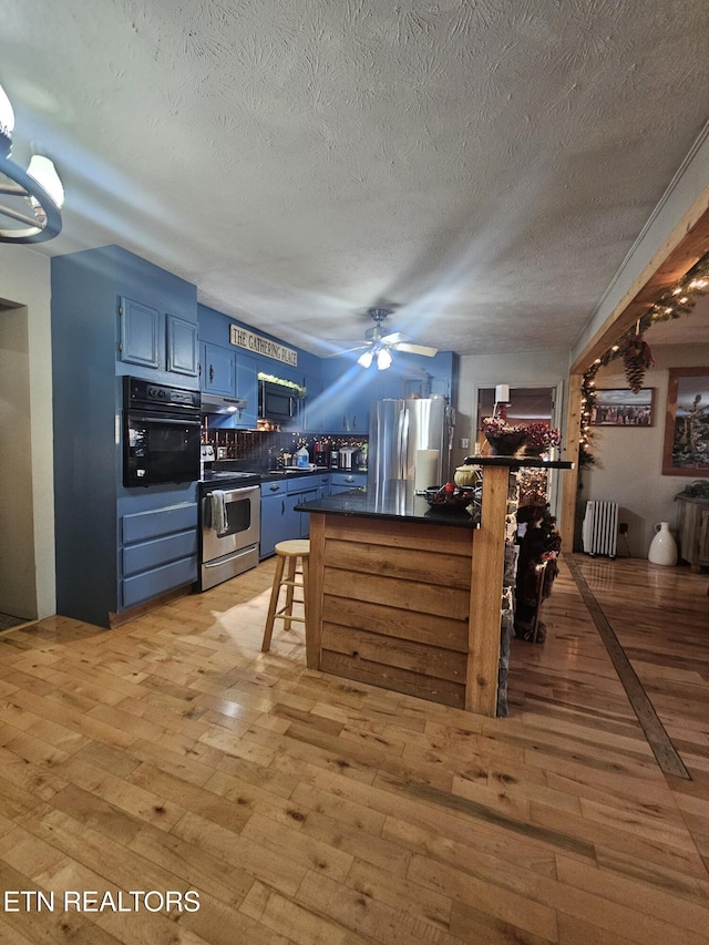 kitchen featuring kitchen peninsula, light wood-type flooring, radiator, black appliances, and blue cabinetry