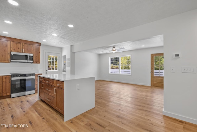 kitchen with appliances with stainless steel finishes, a wealth of natural light, a textured ceiling, and light hardwood / wood-style flooring