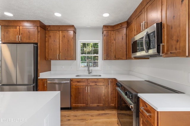 kitchen with sink, a textured ceiling, stainless steel appliances, and light wood-type flooring