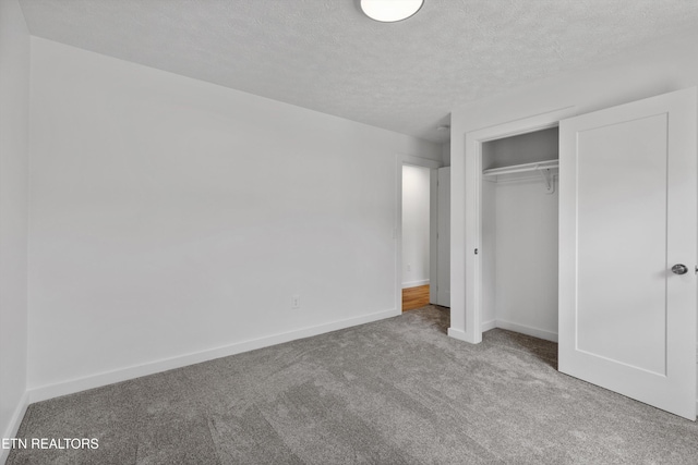 unfurnished bedroom featuring a textured ceiling, a closet, and light colored carpet