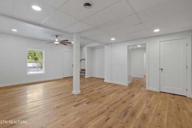 basement with light wood-type flooring, a paneled ceiling, and ceiling fan