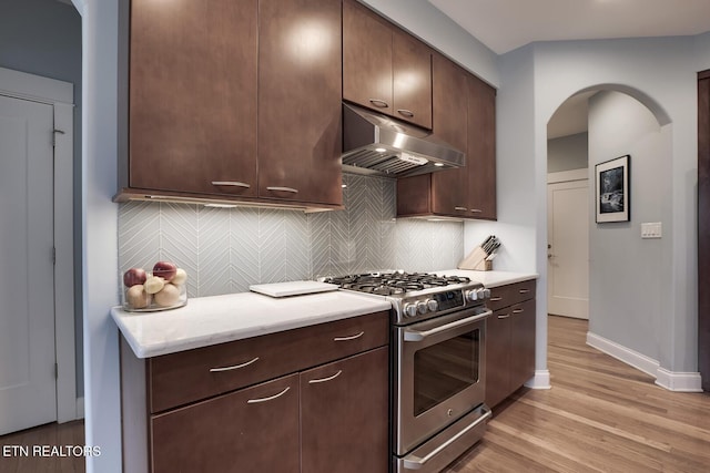 kitchen featuring stainless steel range with gas cooktop, range hood, decorative backsplash, light hardwood / wood-style floors, and dark brown cabinetry