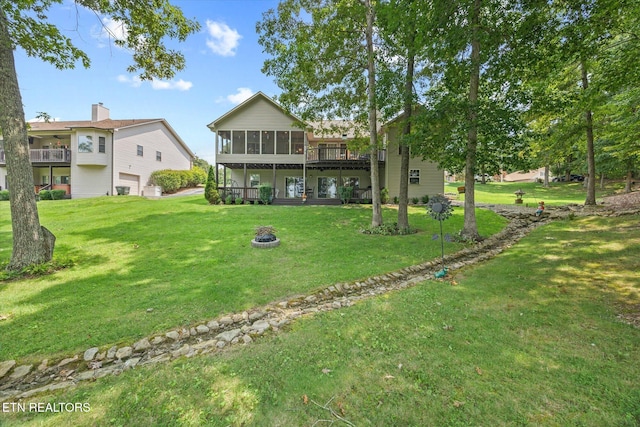 back of property with a lawn, a sunroom, an outdoor fire pit, and a wooden deck