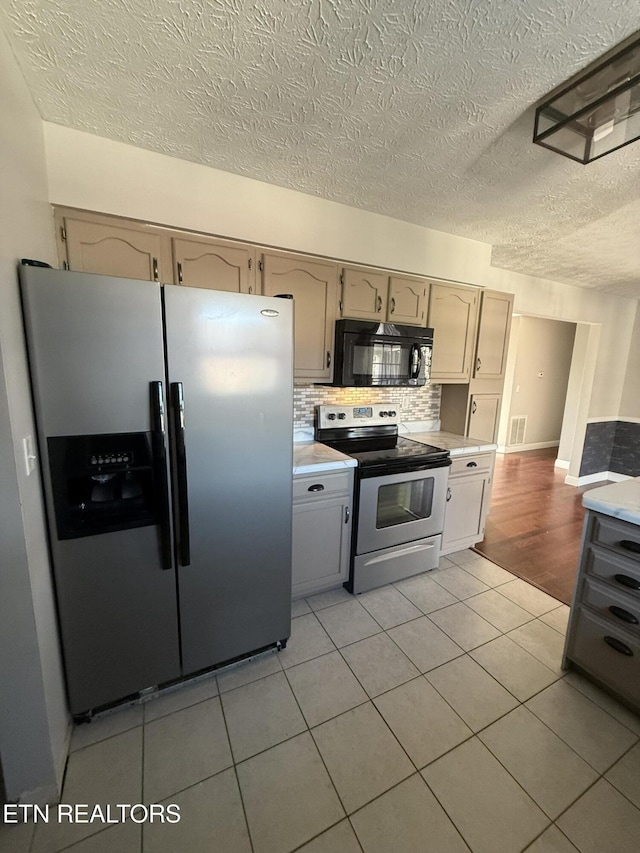 kitchen featuring decorative backsplash, light tile patterned floors, a textured ceiling, and appliances with stainless steel finishes