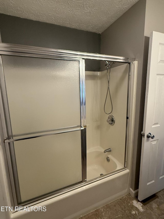 bathroom featuring shower / bath combination with glass door and a textured ceiling