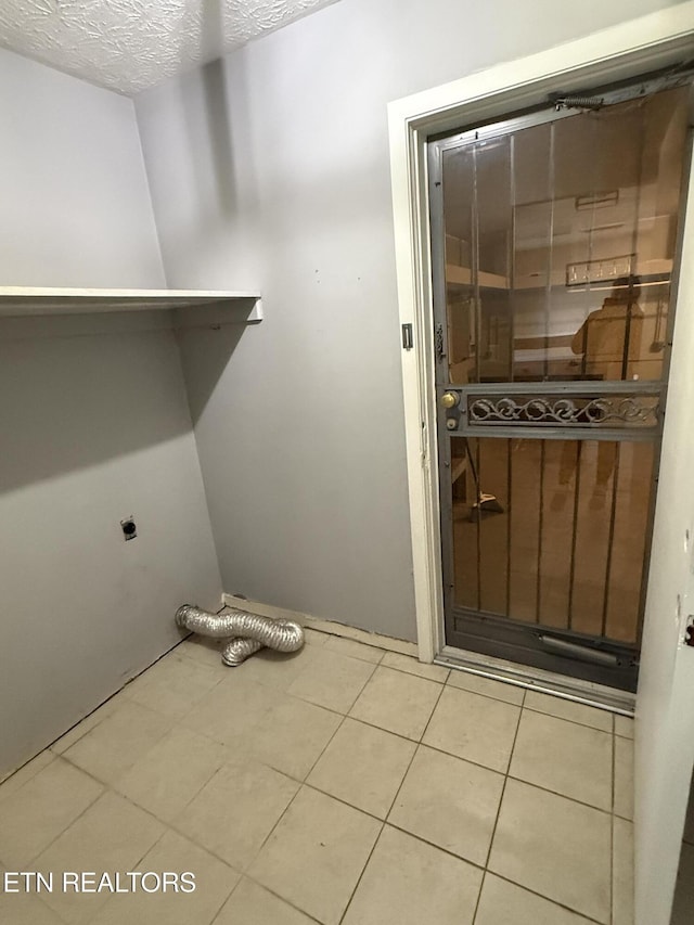 clothes washing area with electric dryer hookup, light tile patterned floors, and a textured ceiling