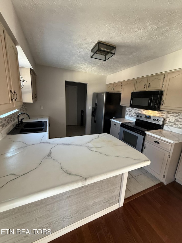 kitchen featuring backsplash, sink, appliances with stainless steel finishes, cream cabinetry, and light hardwood / wood-style floors