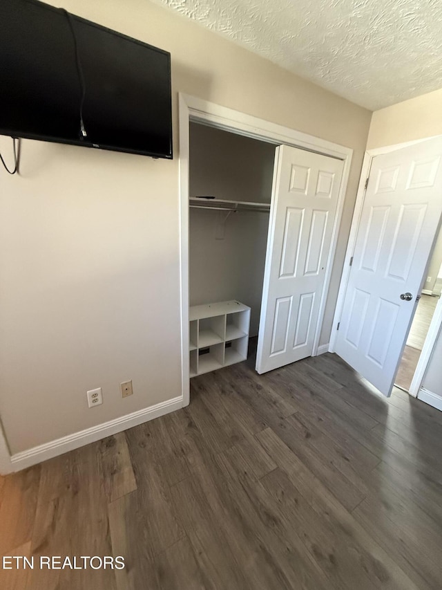 unfurnished bedroom featuring dark hardwood / wood-style flooring, a textured ceiling, and a closet