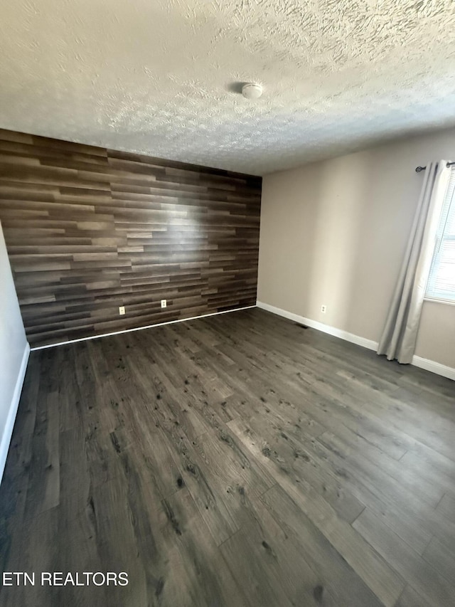 empty room with a textured ceiling, dark wood-type flooring, and wooden walls