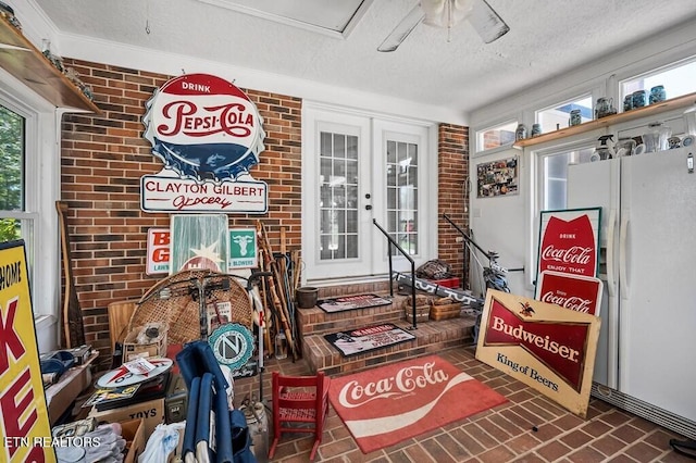 interior space with french doors, ceiling fan, ornamental molding, a textured ceiling, and brick wall