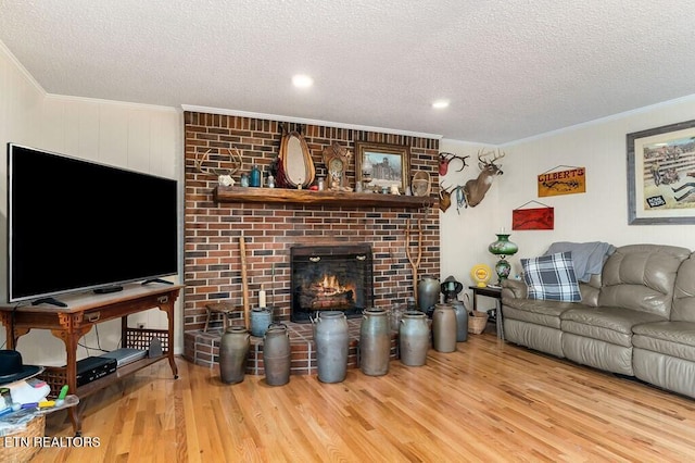 living room featuring a textured ceiling, light wood-type flooring, a brick fireplace, and crown molding