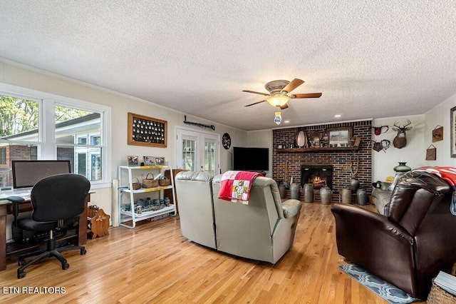 living room featuring a fireplace, a textured ceiling, light wood-type flooring, and ceiling fan