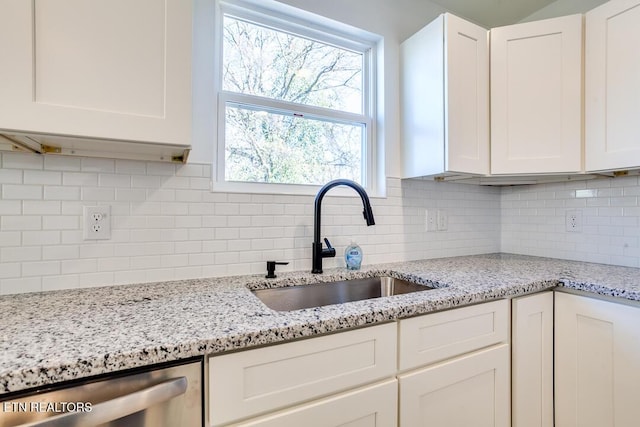 kitchen featuring light stone countertops, backsplash, sink, dishwasher, and white cabinets