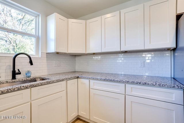 kitchen with tasteful backsplash, light stone countertops, sink, and white cabinets