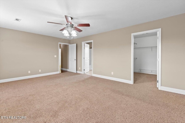 unfurnished bedroom featuring ceiling fan, a walk in closet, light carpet, and a closet