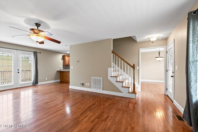 unfurnished living room with french doors, ceiling fan with notable chandelier, and hardwood / wood-style floors