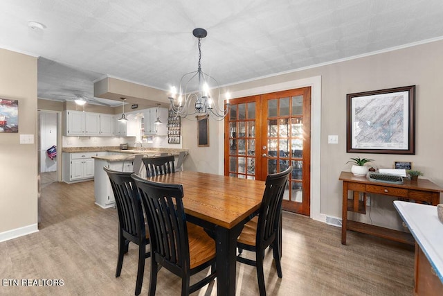 dining area featuring sink, light wood-type flooring, crown molding, and an inviting chandelier