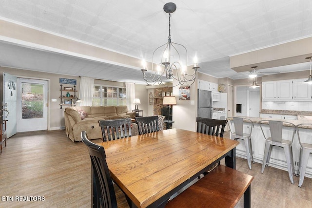 dining space with ceiling fan with notable chandelier, light wood-type flooring, a brick fireplace, and plenty of natural light