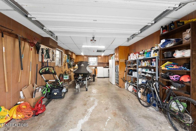 garage with washing machine and clothes dryer, wood walls, and white refrigerator