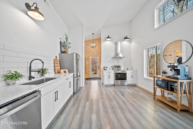 kitchen featuring sink, wall chimney exhaust hood, hanging light fixtures, stainless steel appliances, and white cabinets