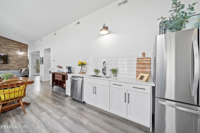 kitchen with wood walls, sink, appliances with stainless steel finishes, light hardwood / wood-style floors, and white cabinetry