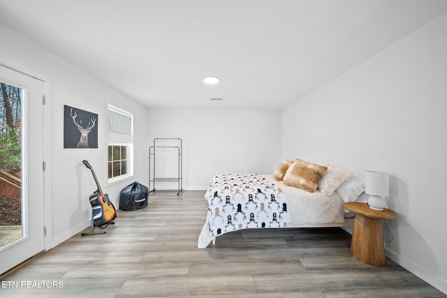 bedroom featuring access to exterior, light hardwood / wood-style flooring, and multiple windows