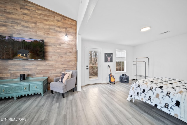 bedroom with light hardwood / wood-style floors, vaulted ceiling, and wood walls