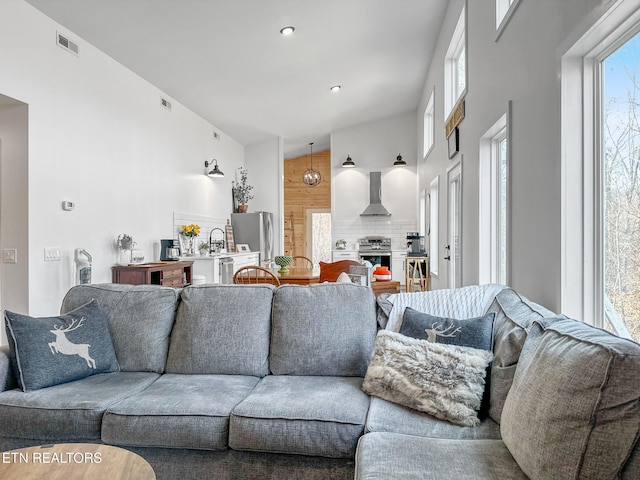 living room featuring wooden walls, high vaulted ceiling, and a healthy amount of sunlight