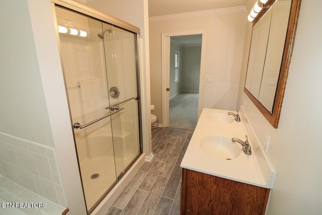 bathroom featuring vanity, toilet, a shower with door, and crown molding