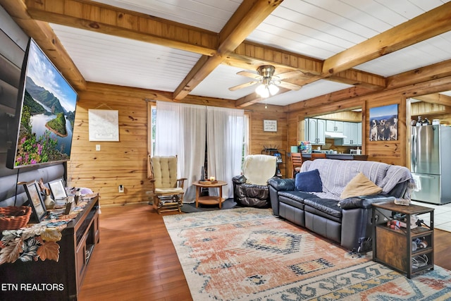 living room with beamed ceiling, ceiling fan, wood walls, and dark wood-type flooring