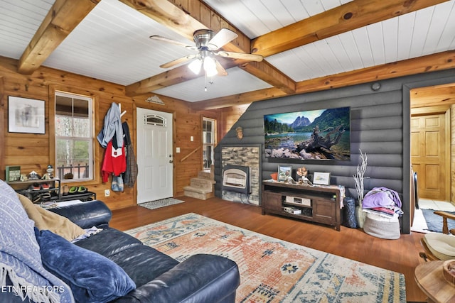 living room featuring dark hardwood / wood-style floors, beam ceiling, a stone fireplace, and ceiling fan