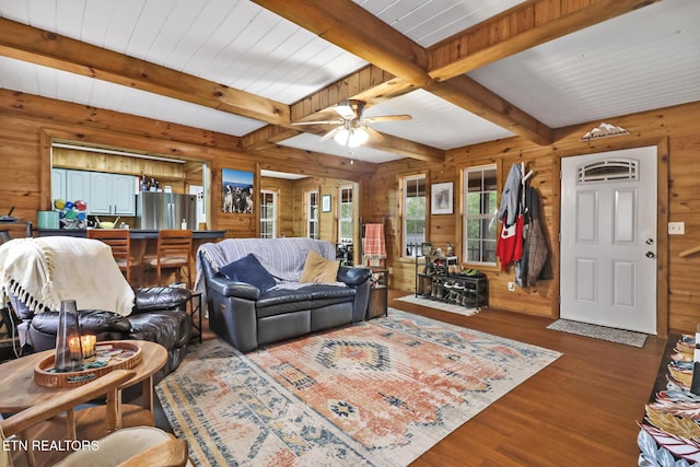 living room with beam ceiling, dark hardwood / wood-style flooring, ceiling fan, and wooden walls