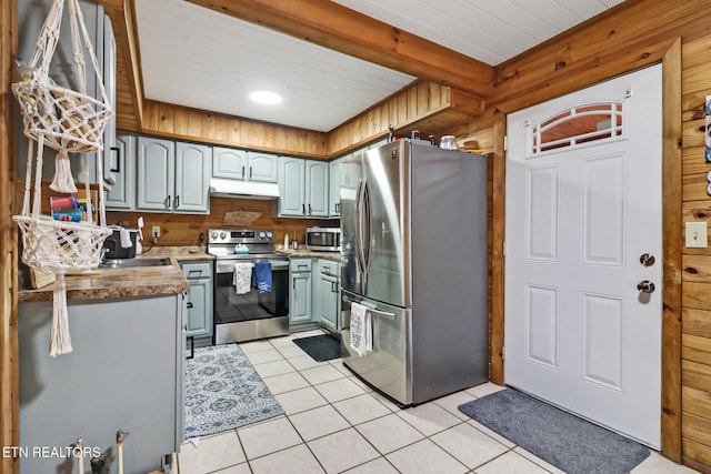 kitchen with wood walls, light tile patterned flooring, and stainless steel appliances