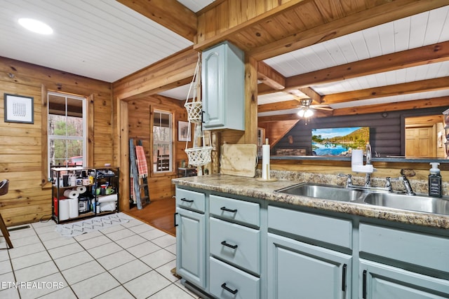 kitchen featuring beam ceiling, ceiling fan, sink, wooden walls, and light tile patterned floors